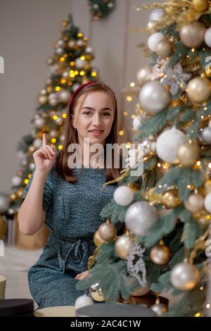 Bella ragazza decorare albero di Natale. Una giovane donna sorridente prepara un albero di Natale per la vacanza. Lussureggiante verde albero di Natale con palline dorate Foto Stock