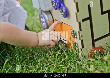 Carino bambina sta giocando con busiboard all'aperto sull'erba verde. Giocattoli educativi per i bimbi. ragazza porta aperta a cubo del bordo Foto Stock