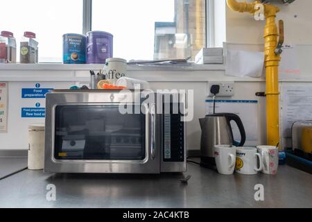 Un forno a microonde, bollitore elettrico e tazze di sedersi su un piano di lavoro in acciaio inox in una scuola di cucina. Foto Stock