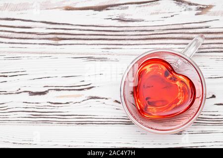 Vista superiore della red hibiscus tea in vetro a forma di cuore sulla tazza bianca tavolo in legno Foto Stock