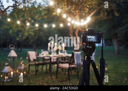 Attrezzature professionali. La fotocamera sul treppiede in campo nella parte anteriore della tavola imbandita al tempo di sera Foto Stock