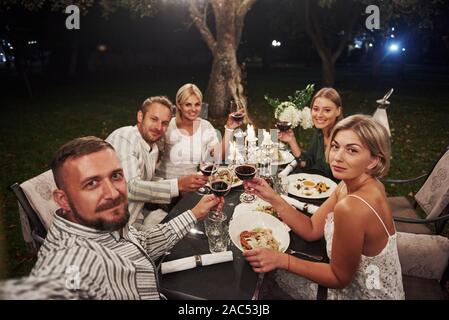 Ragazzo prende selfie. Gruppo di amici nella elegante usura cena di lusso Foto Stock