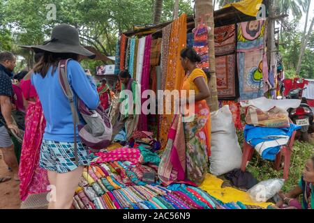 Western tourist shopping per saries ad Anjuna Mercoledì Mercato in Goa, India Foto Stock