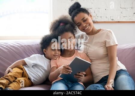 Felice biracial mamma e bimbi piccoli rilassarsi utilizzando tablet Foto Stock