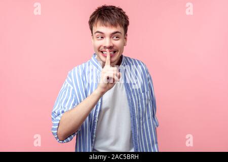 Funny segreto, non dite a nessuno!!!! Ritratto di positivo i capelli castani uomo con piccola barba e baffi in camicia che mostra il silenzio gesto, guardando a parte. Foto Stock