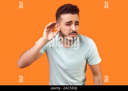 Non riesco a sentire voi! Ritratto di nosy brunette uomo con la barba bianca t-shirt cercando di ascoltare pettegolezzi, tenendo la mano vicino a orecchio e ascolto attento auto Foto Stock