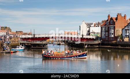 Una barca turistica è raffigurato sul fiume Esk nella cittadina balneare di Whitby, Yorkshire in Inghilterra settentrionale. In fondo è Whitby ponte girevole. Foto Stock