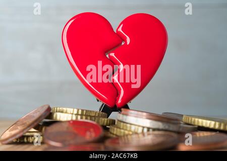 Rosso rotto il giorno di San Valentino cuore su una pila di monete in euro. Amore e Denaro problemi concetto astratto. Sfondo grigio. Foto Stock