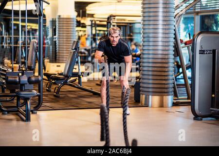 L'uomo rafforza i muscoli addominali e i muscoli del braccio in palestra con swing corda. Foto Stock