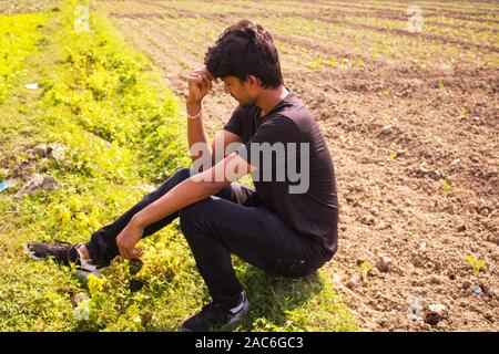 Un giovane ragazzo è seduta sul campo e pensare profondamente o in tensione, lo sfondo è la natura Foto Stock