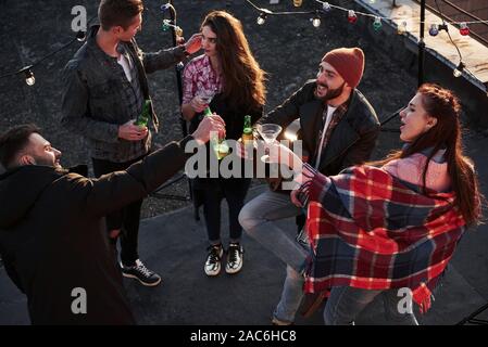 Partito in pieno svolgimento. Vista dall'alto di giovani amici che bere, suonare la chitarra e divertirsi in corrispondenza del tetto con una decorazione colorata delle lampadine Foto Stock