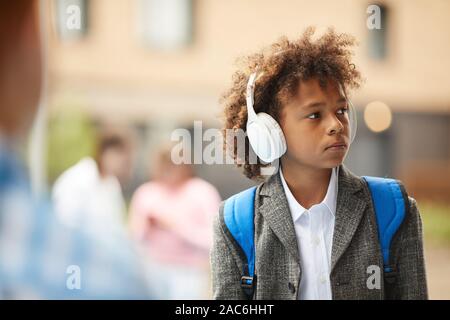 Scolaro africana di indossare le cuffie per ascoltare musica mentre si cammina sulla strada dopo la scuola Foto Stock