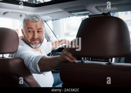 Buon umore. Alla guida di una vettura in retromarcia. Guardando dietro. L uomo nella sua nuovissima automobile Foto Stock