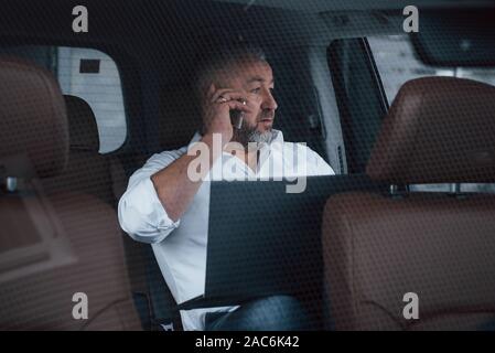 Parlando di alcune trattative. Avente attività chiamata mentre seduti sul retro della vettura con argento notebook colorato Foto Stock