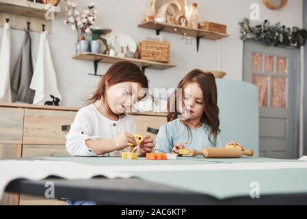 Tempo libero quando i genitori non è a casa. Due ragazzi che giocano con il colore giallo e arancio dei giocattoli nella cucina bianca Foto Stock