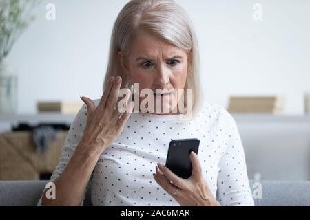 Mad donna anziana smartphone di contenimento avente problema con gadget Foto Stock