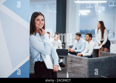 Contando sulla parete. Ritratto di giovane ragazza sta in ufficio con i dipendenti a sfondo Foto Stock