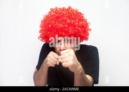 Ritratto di funny man con setole e ricci parrucca rosso clenching pugni in lotta gesto, pronti ad attaccare o difendersi, ha comico volto minaccioso Foto Stock