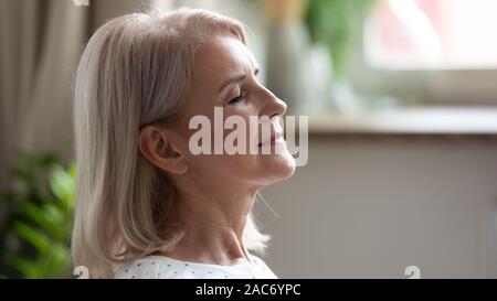Closeup calma 50s donna occhi chiusi godere di fine settimana in ambienti interni Foto Stock