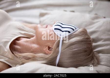 Closeup 50s donna matura indossando maschera dormire sdraiati a letto Foto Stock