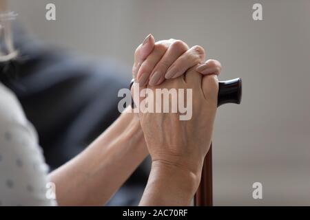 Primo piano immagine femmina vecchie mani bastone seduto al chiuso Foto Stock