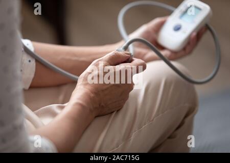 Closeup donna età dello sfigmomanometro utilizzando il controllo della pressione arteriosa a casa Foto Stock
