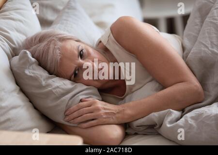 Triste anziani donna giaceva a letto soffre di insonnia Foto Stock