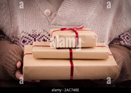 Confezioni regalo con nastro rosso nelle mani. Tenere le mani doni nella carta craft Foto Stock