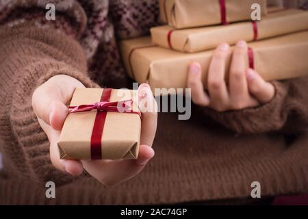 Mano trattiene una confezione regalo. Ragazza in un maglione può contenere una pila di confezioni regalo in un marrone carta craft. Foto Stock