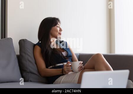 Stanco imprenditrice asiatici in appoggio a guardare fuori dalla finestra di bere il caffè Foto Stock
