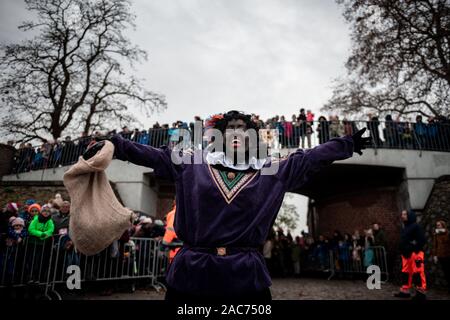 Krefeld, Germania. 01 Dic, 2019. Un 'Zwarter Piet' saluta il pubblico. Il Sinterklaas (Nicholas) da Venlo arriva con diversi "Zwarten Piets" (Black Peter) in scia a Steiger in Krefeld in barca. Tradizionalmente, 'Zwarten Piets' distribuire caramelle ai bambini. Nei Paesi Bassi il dipinto di nero aiutanti di Sinterklaas sono ora controversa. Un paio di giorni fa vi sono state proteste con molti arresti di Apeldoorn. Credito: Fabian Strauch/dpa/Alamy Live News Foto Stock