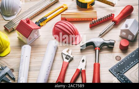 Costruzione, casa di ristrutturazione concetto. Utensili a mano, elmetti e progetto blueprint su legno, vista ravvicinata Foto Stock