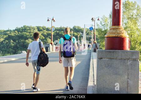 Stile di vita dei giovani maschi, adolescenti con zaini a piedi le spalle a piedi ponte sul fiume, soleggiata giornata estiva Foto Stock