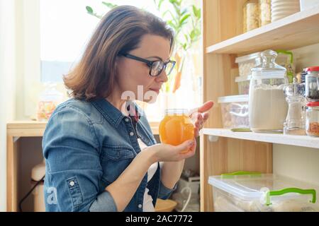 Una donna con un vasetto di golden organico miele freschi nella cucina vicino al cibo per rack di archiviazione Foto Stock