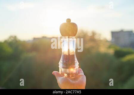 Pepe nero piselli in un mulino in mano womans, sfondo tramonto, serale città Foto Stock