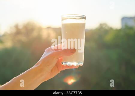 Vetro con latte in mano womans, sfondo tramonto, serale città Foto Stock