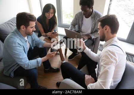 Lavoratori multietnica seduti in cerchio usando diversi gadget mobile Foto Stock