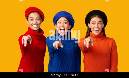 Sorridente diverse ragazze dita di puntamento in Telecamera, sfondo giallo, Panorama Foto Stock