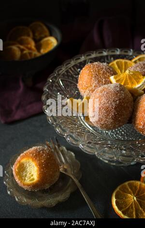 Dark e moody fotografia cibo speziato di ciambella arancione fori con lo zucchero Foto Stock