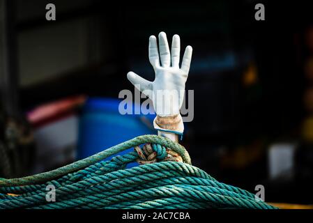 Bianco Guanto in gomma su un bastone come una mano sollevata al di sopra di un turchese fune su una barca da pesca nel porto di Cres, Croazia Foto Stock