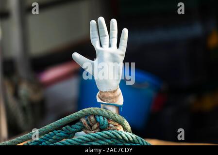 Bianco Guanto in gomma su un bastone come una mano sollevata al di sopra di un turchese fune su una barca da pesca nel porto di Cres, Croazia Foto Stock