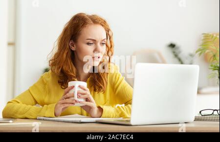 Malinconici imprenditrice di bere caffè, lavorando sul computer portatile Foto Stock