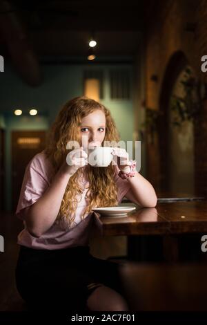 Una ragazza di bere il cappuccino all'interno di un coffee shop. Foto Stock