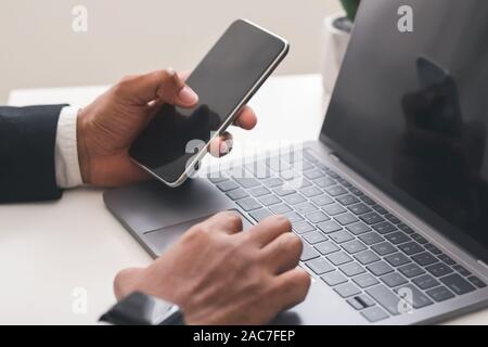 Imprenditore utilizza lo smartphone con lo schermo è vuoto e di lavoro sul computer portatile Foto Stock