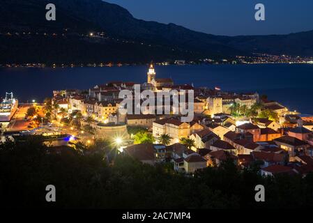 Vista di strade medievali e gli edifici dell'illuminato storica Vecchia città di Korcula di fronte all'isola di Peljesac dopo il tramonto, Croazia Foto Stock