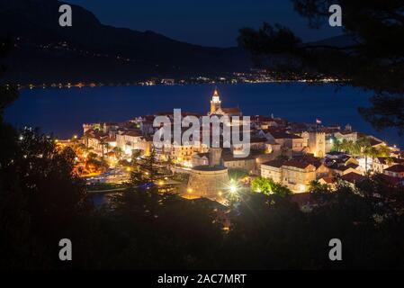 Vista di strade medievali e gli edifici dell'illuminato storica Vecchia città di Korcula di fronte all'isola di Peljesac dopo il tramonto, Croazia Foto Stock