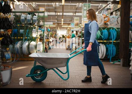 Venditore femmina in grembiule detiene il giardino carrello in negozio Foto Stock