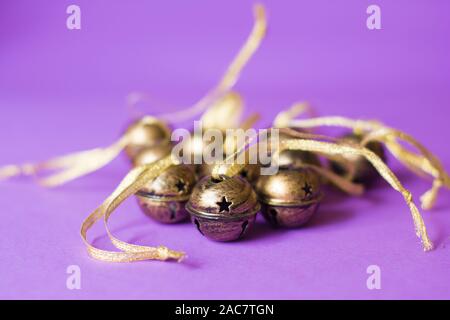 Mazzetto di ottone sleigh bells decorazioni con glitter nastri su uno sfondo violetto. Foto Stock