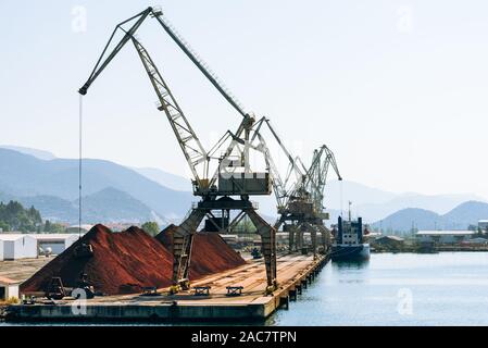 Il caricamento con gru di cucchiaia escavatore in una pila di minerale di ferro ad una banchina di carico nel porto di Ploče, Dalmazia, Croazia Foto Stock