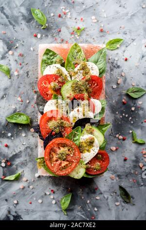 Insalata caprese con mozzarella, cimelio di pomodori, cetrioli, basilico e pesto servito su sale rosa blocco su sfondo grigio vista dall'alto uno spazio di copia Foto Stock